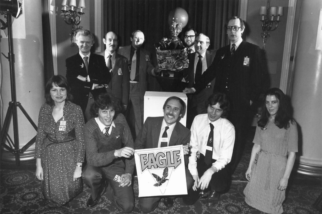 Fleetway staff at the launch of New Eagle in 1982 at the Waldorf Hotel, London, stage managed by Barrie Tomlinson.  Top Row, left to right: Jack Cunningham (art staff), John Jackson (art staff), Doug Church (art editor), the Mekon, Roy Preston (writer), Sid Bicknell (Fleetway editor), then Barrie Tomlinson, standing. Bottom Row, left to right: Barrie's secretary, Debbie Watts; Paul Bensberg (art staff);  David Hunt, holding the Eagle logo; Ian Rimmer (assistant editor); and Janet Dixon (sub editor). Photo courtesy Barrie Tomlinson