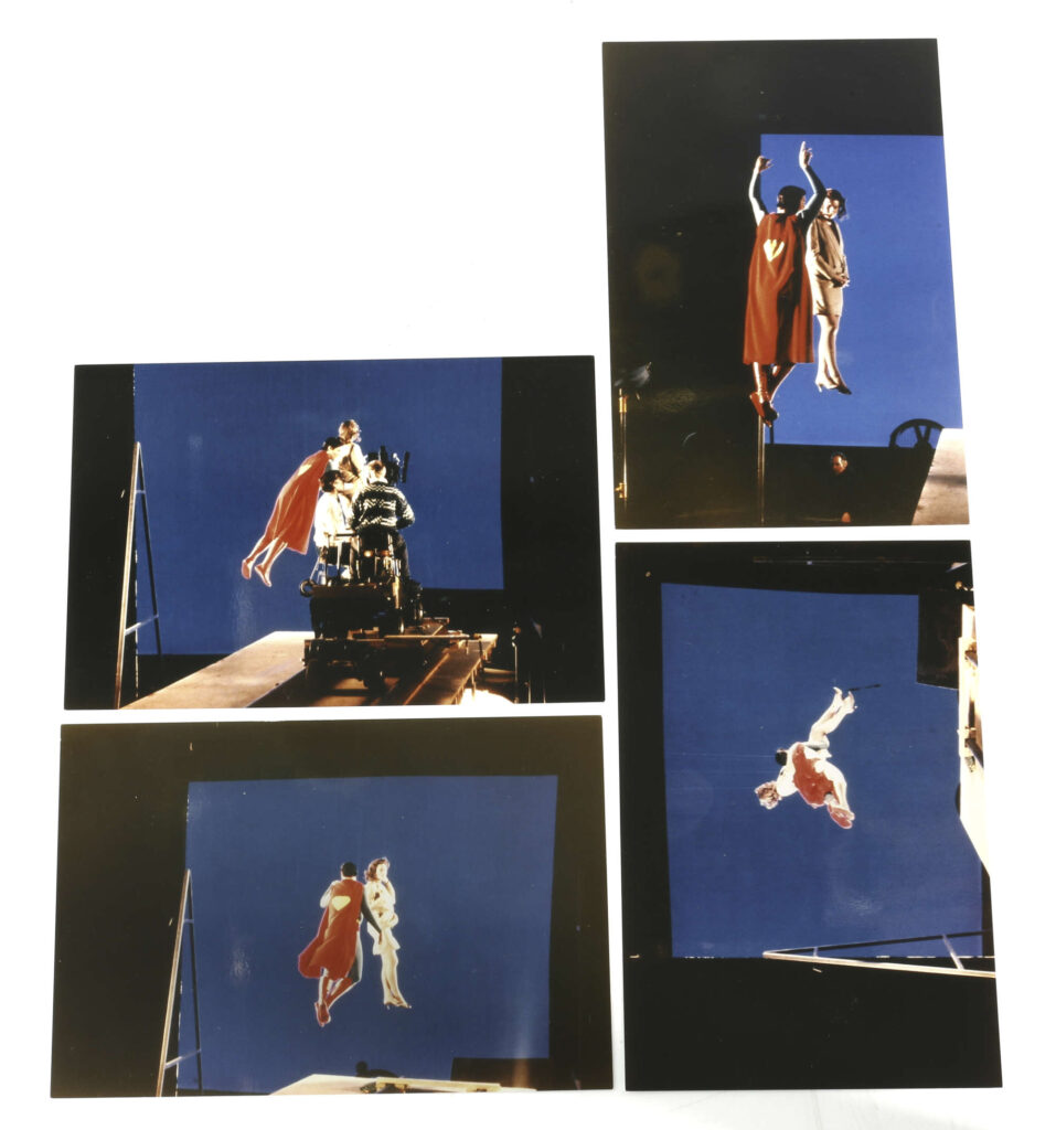 Superman (1978) behind-the-scenes Special Effects photographs. A group of four colour photographs, depicted Christopher Reeve in character dressed as Superman with possibly a stand-in or stunt-double, the actors dangled from hidden wires and safety harnesses as the cameraman films them from a rostrum rehearsing various flying shots against a blue screen, 6 x 4 inches.