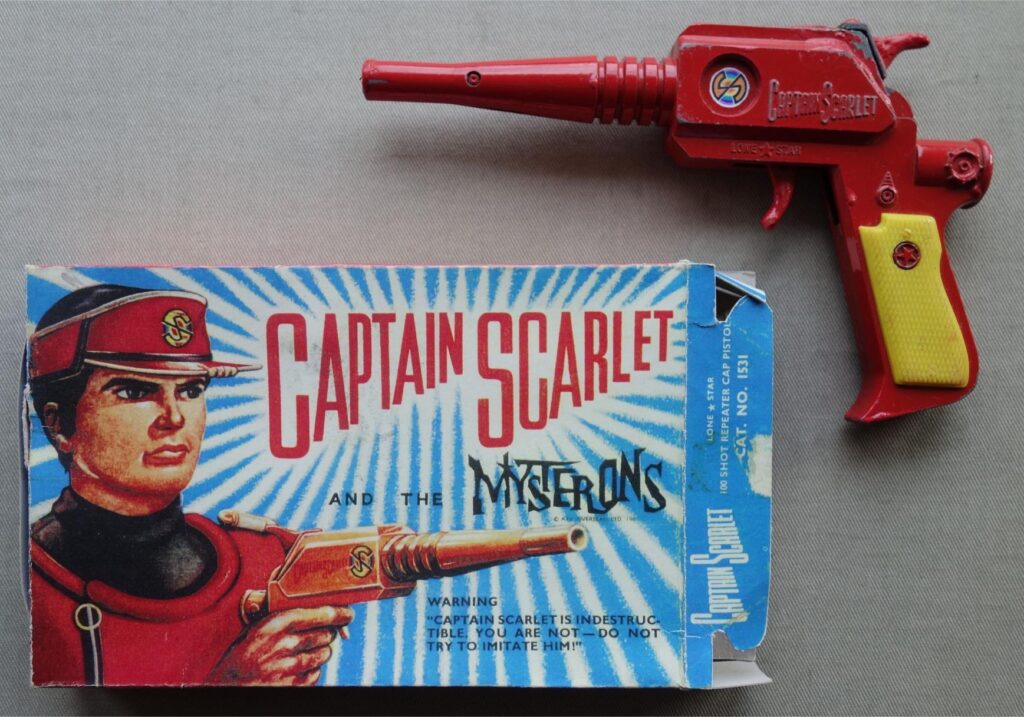 Captain Scarlet and the Mysterons Metal Toy Lone Star 1960s in Reproduction Box. An original metal toy from the 1960s, produced by Lone Star. It measures approx 185 x 115 x 20 mm and has vibrant colours. It originally fired caps. The trigger mechanism still works and the top flips out to re-load, should you wish. Untested. 