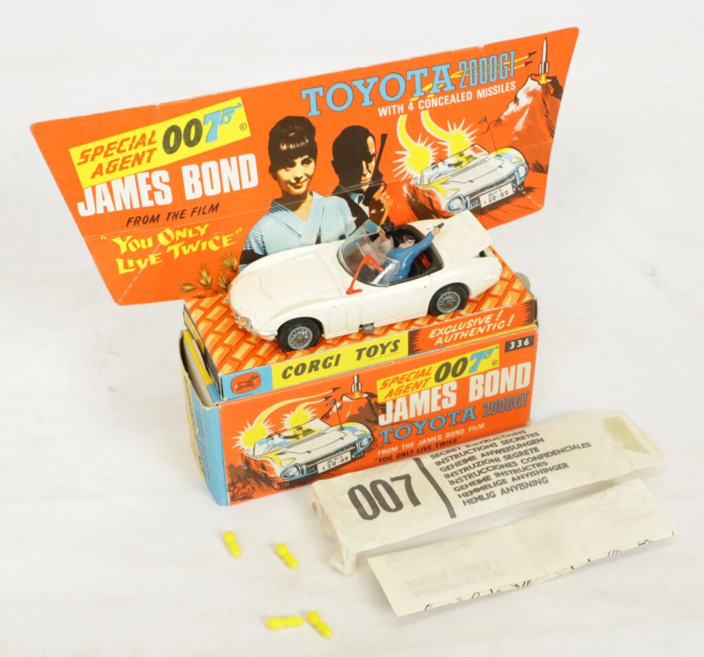 Corgi Toys 336 James Bond Toyota 2000GT from the film You Only Live Twice, comprising a white vehicle with seated figures, four yellow missiles, a complete secret instruction envelope with paper leaflet, and an inner pictorial display stand, all contained within an excellent to near mint illustrated card box.