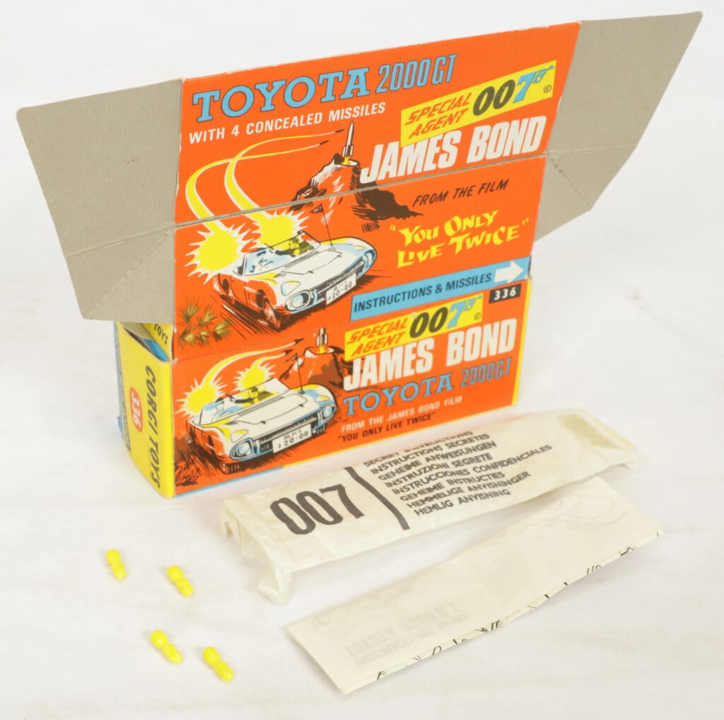 Corgi Toys 336 James Bond Toyota 2000GT from the film You Only Live Twice, comprising a white vehicle with seated figures, four yellow missiles, a complete secret instruction envelope with paper leaflet, and an inner pictorial display stand, all contained within an excellent to near mint illustrated card box.