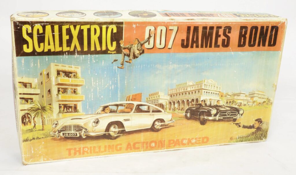 Scalextric vintage 007 James Bond slot car racing set including curved track sections, red and blue hand controllers, incorrect slot cars in red and yellow, scenery components, and instructions