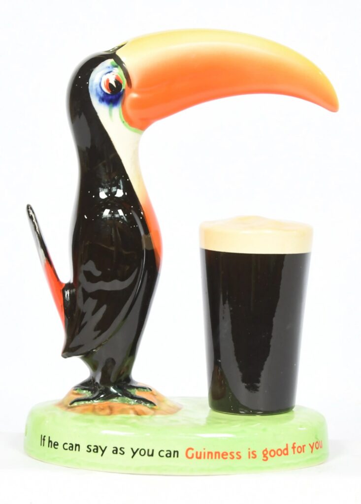 Carlton Ware Guinness Toucan Lamp Base – a vintage 1950s ceramic advertising lamp base modelled as a toucan standing beside a pint of Guinness. The green oval base is printed with the slogan 'If he can say as you can Guinness is good for you'.